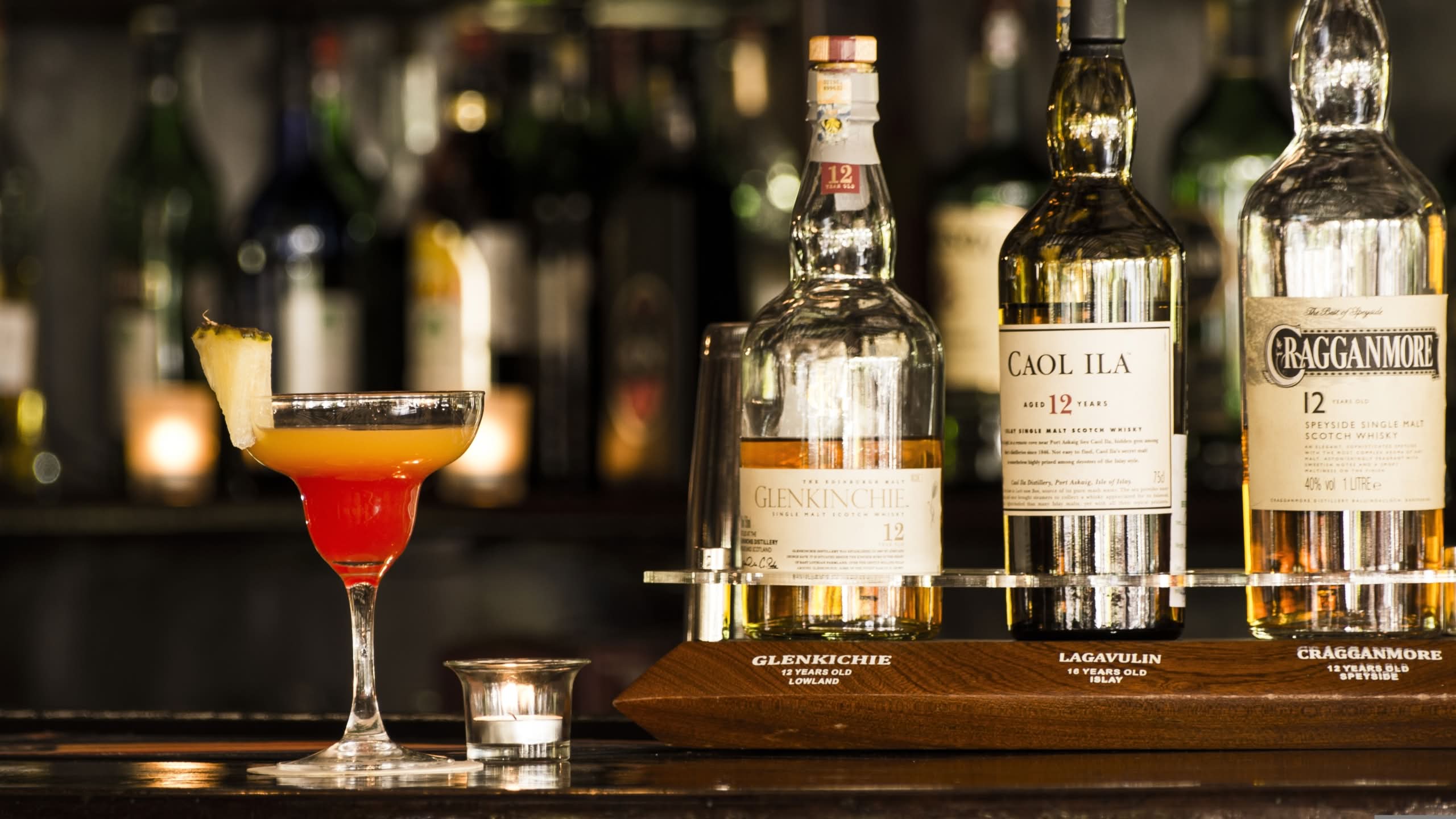 Scotch whisky bottles on a bar tasting board next to a whisky cocktail with pineapple garnish